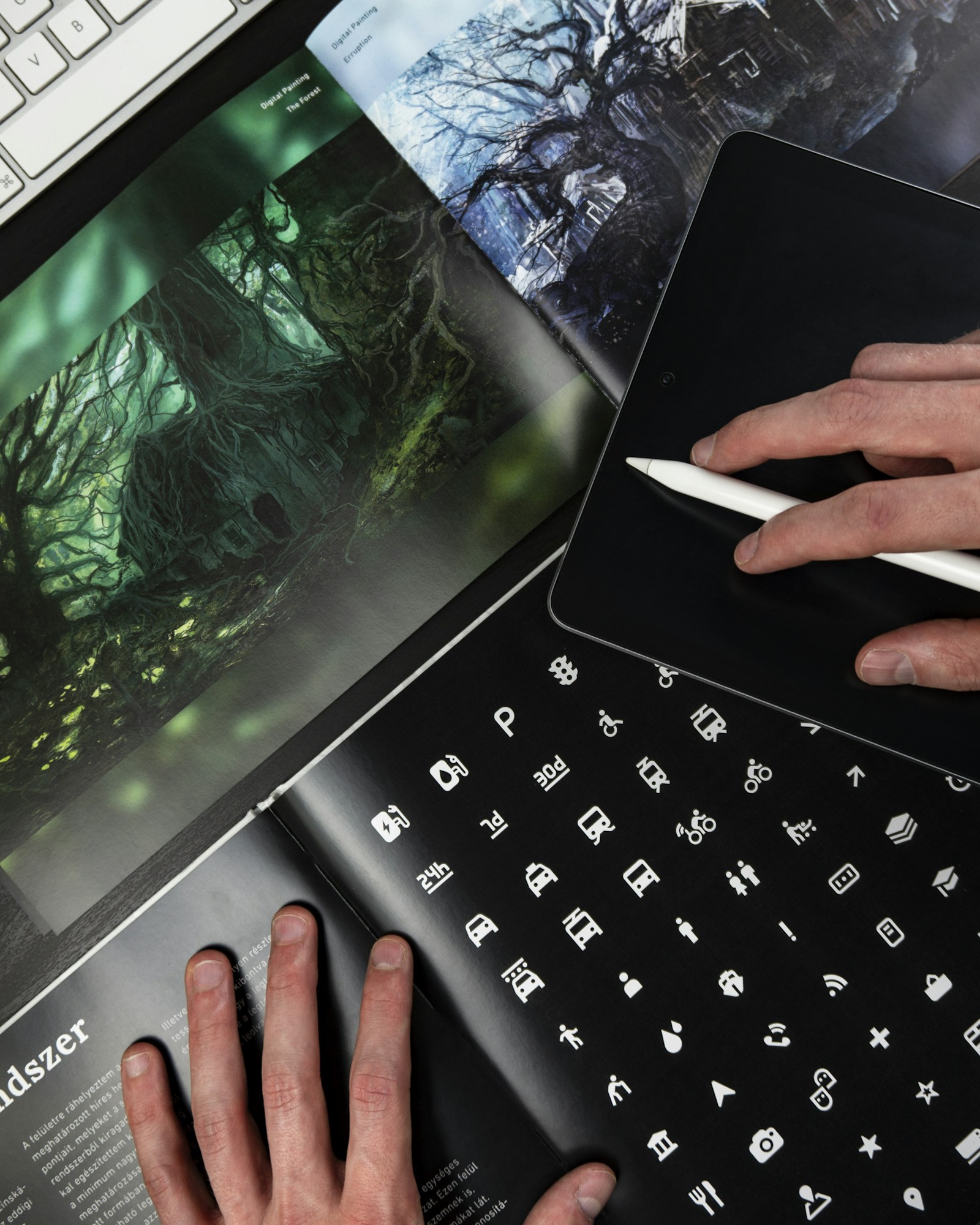 Hands working across a tablet, keyboard, and visual reference book